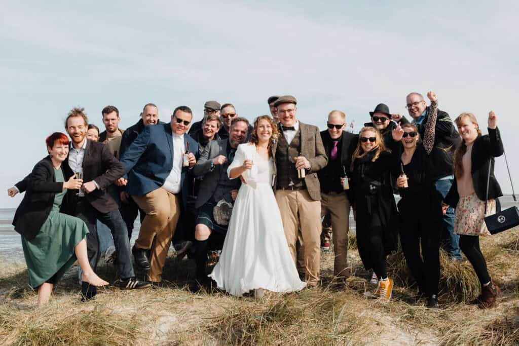 Brautpaar feiert ausgelassen mit Familie und Freunden am Strand.