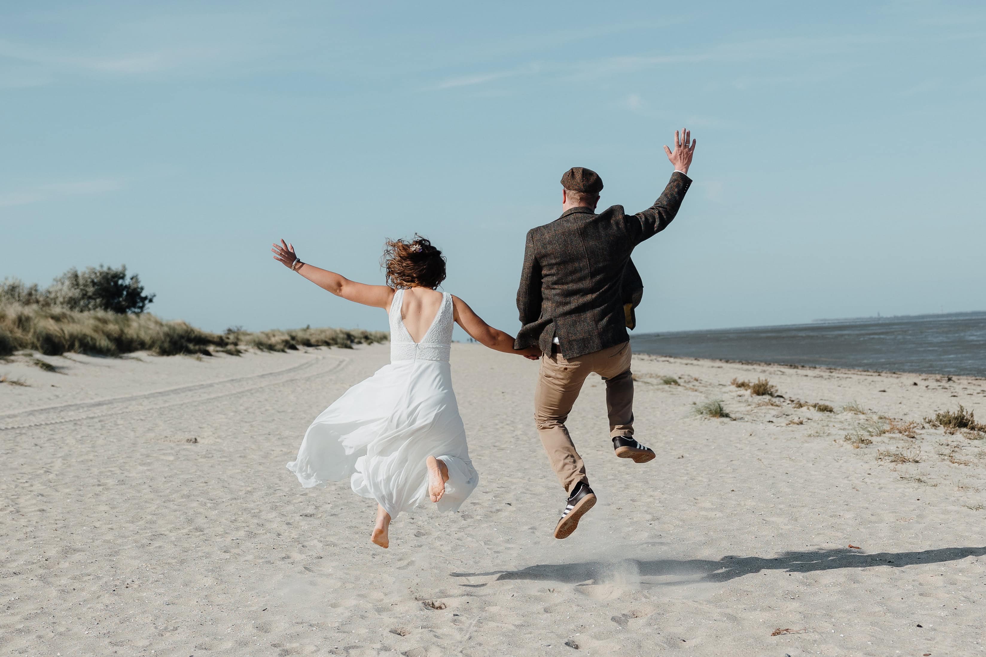 Brautpaar springt ausgelassen am Strand während einer Hochzeit in Schleswig-Holstein.