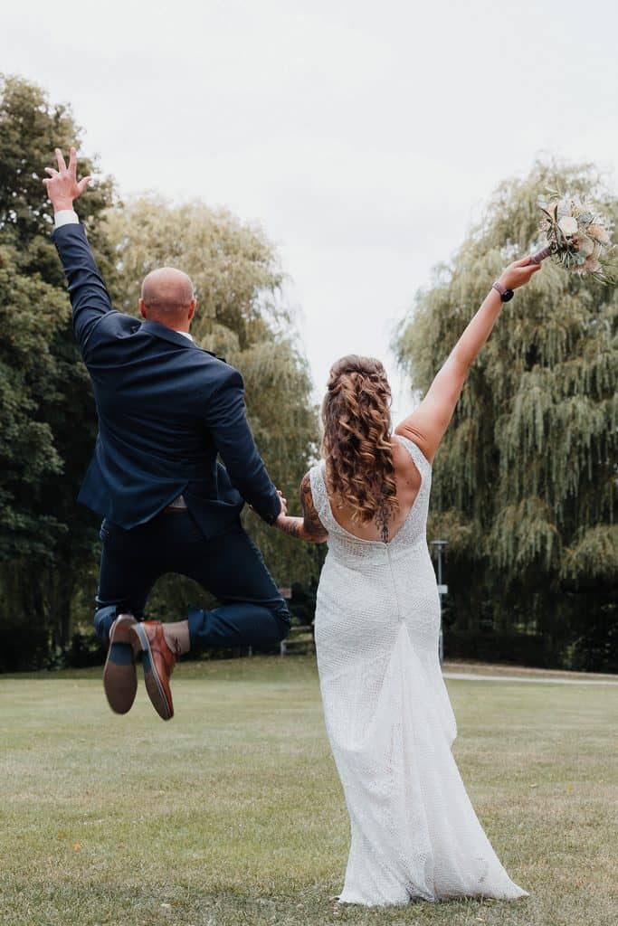Bräutigam springt vor Freude, Braut jubelt beim Paarshooting nach der Hochzeit
