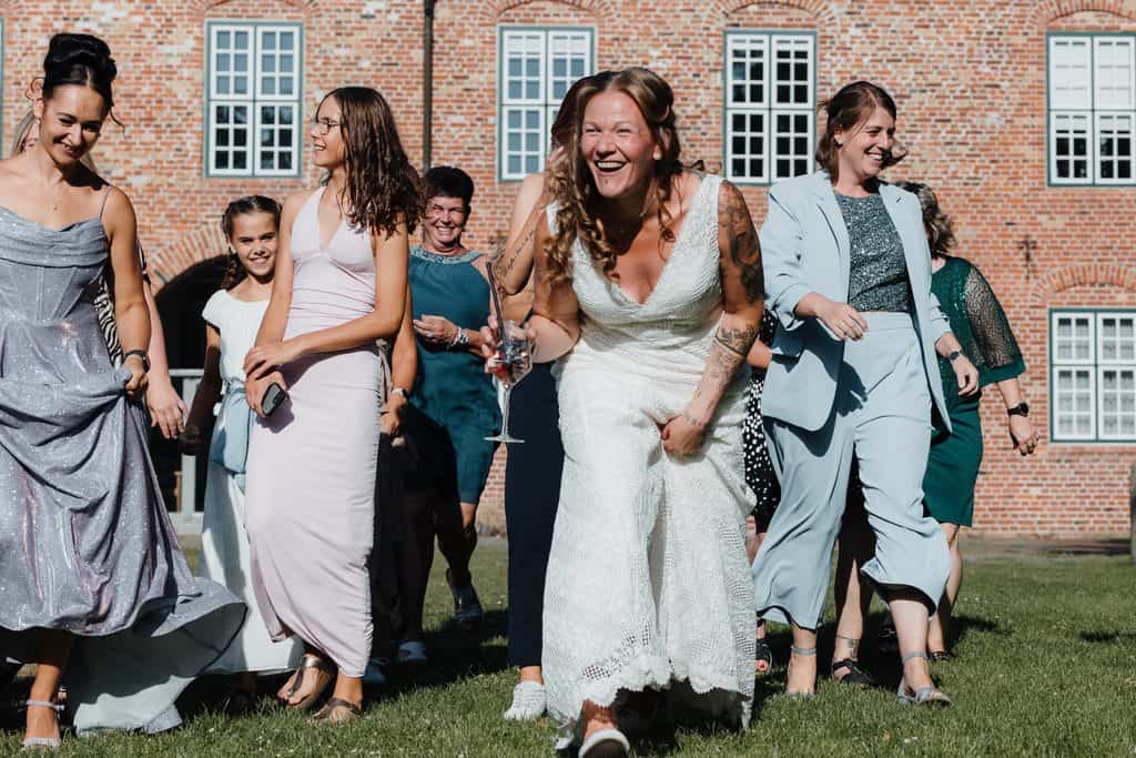 Lachende Braut mit ihren Gästen bei einer Hochzeit im Freien.